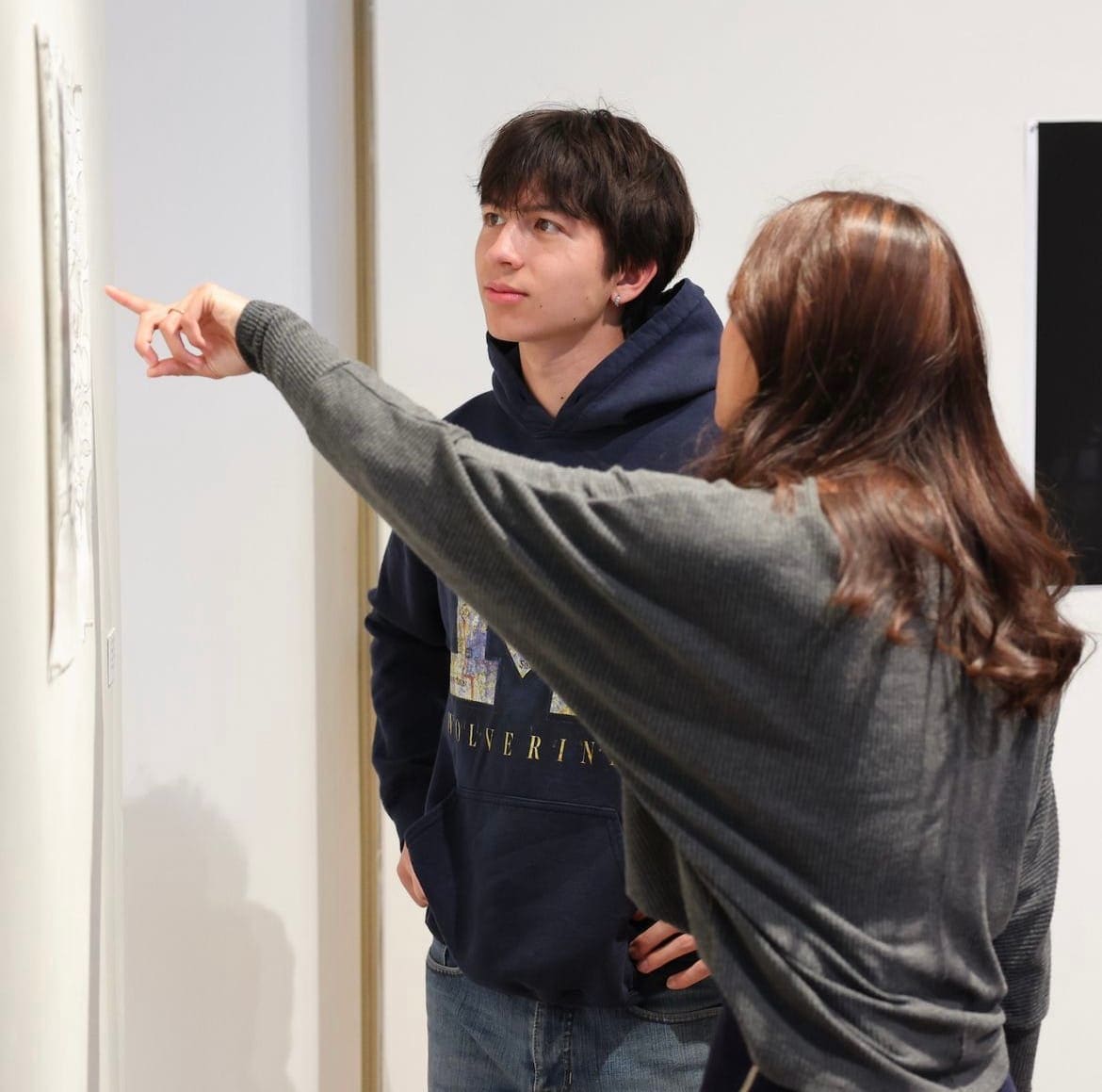 Connor looking at artwork in a gallery as someone points to a piece