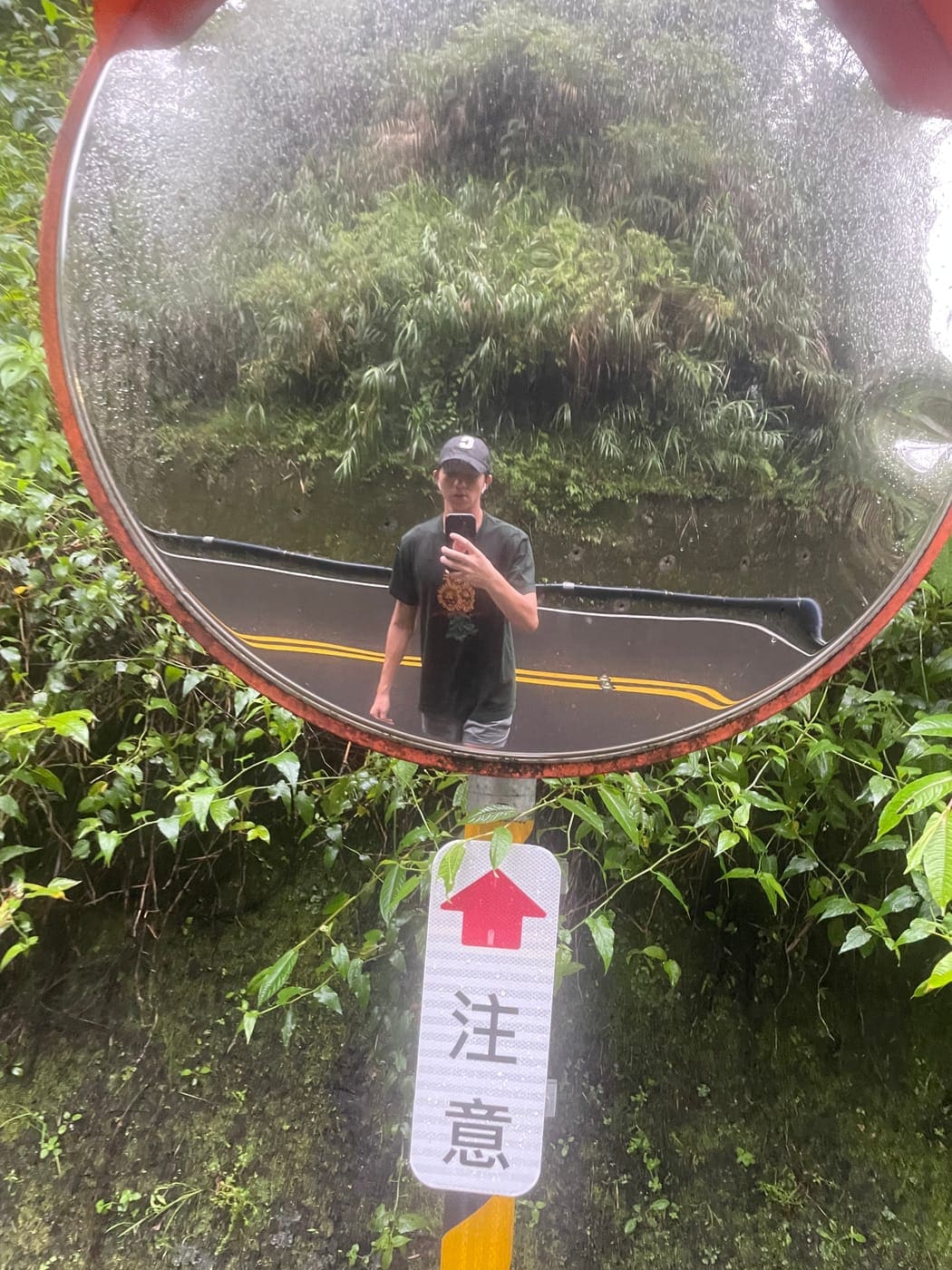Connor's reflection in a roadside mirror on a rainy mountain road
